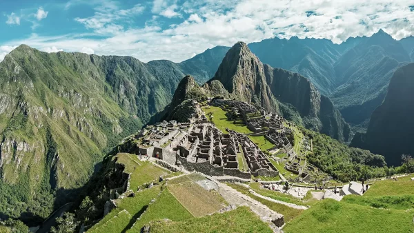 Vista de Machu Picchu de manera panorámica, grandes montañas rodeando la ciudadela inca y en la parte baja se ven los vestigios incas