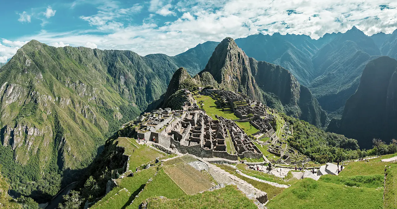 Vista de Machu Picchu de manera panorámica, grandes montañas rodeando la ciudadela inca y en la parte baja se ven los vestigios incas