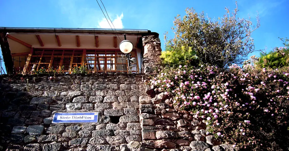 Calle siete diablitos en cusco, árbol con flores rosas hacia afuera y le cartel del nombre de la calle