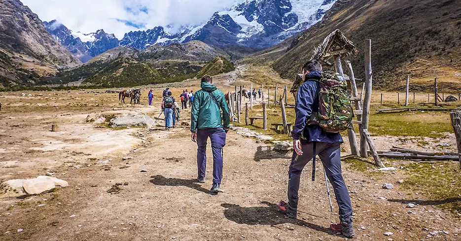 Personas caminando hacia el nevado salkantay con vistas de montañas con nieve y caminos llenos de color verde y caballos mejor trekking en Perú