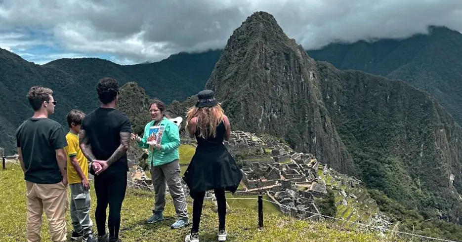 Machu Picchu En Un Día: Ruta Rápida para No Perderte lo Mejor 7 Guía de turismo explicando a los turistas sobre Machu Picchu, al fondo podemos observar los vestigios incas de la ciudadela y las montañas por todos lados