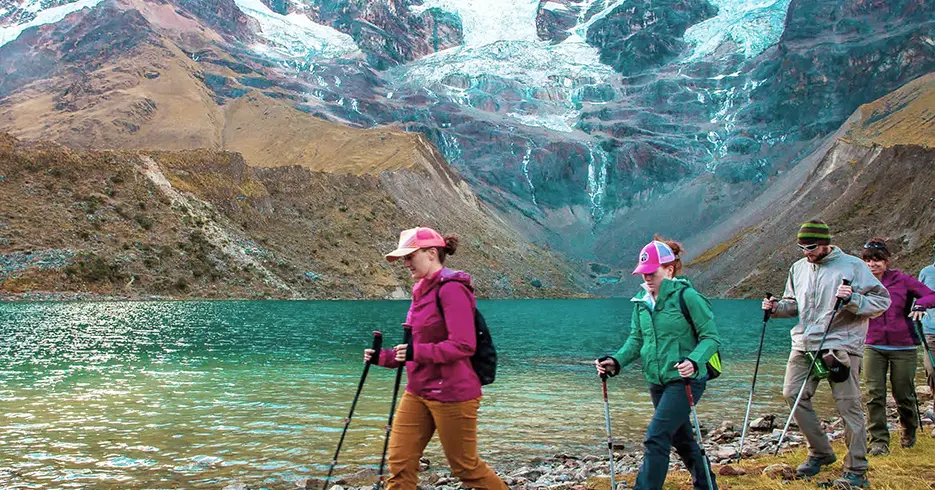 Turistas en un trekking con sus bastones en la laguna humantay, agua cristalina y turquesa y el nevado humantay en la parte de arriba