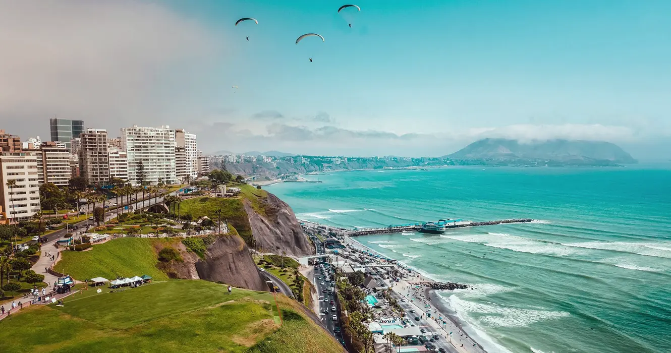 Perú en 10 días: Tu Guía a los mejores lugares 2 La capital de Perú, Lima Miraflores, se puede ver el océano pacífico 3 paracaidistas en el cielo, un cielo despejado celeste, varis carros y personas.