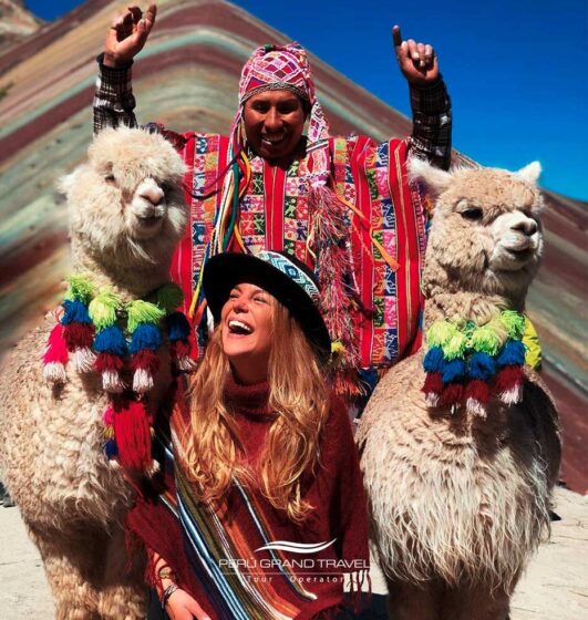 Turista sonriente junto a llamas y un poblador local en la Montaña de 7 Colores, Cusco Perú, experiencia cultural andina