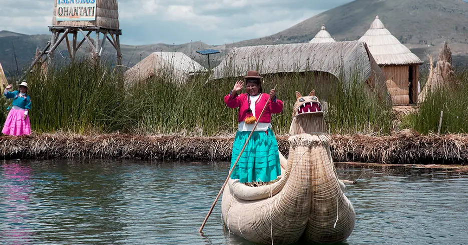 Mujer saludando sobre un barco hecho de totora en la isla de los uros en puno