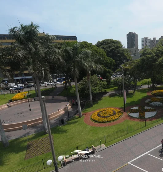 Vista do Parque Kennedy em Miraflores com jardins, visitantes e gatos descansando ao sol.