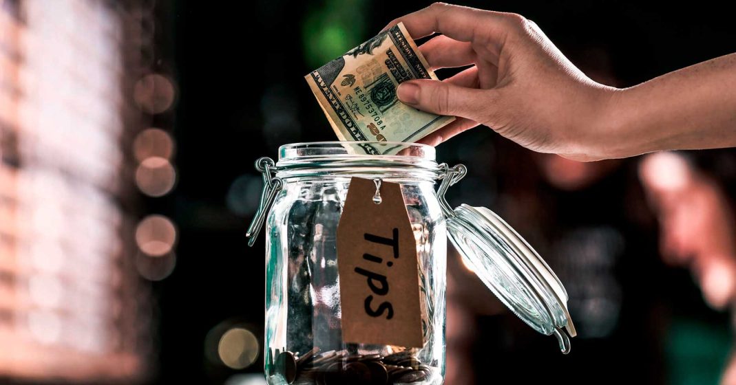 Mano dando propina de 20 dolares en un envase de vidrio