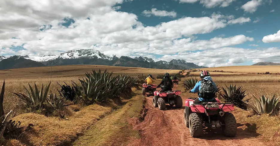 Ruta a las salineras de maras en cuatrimotos con vista de un nevado al fondo y plantas de la zona y un cielo azul despejado