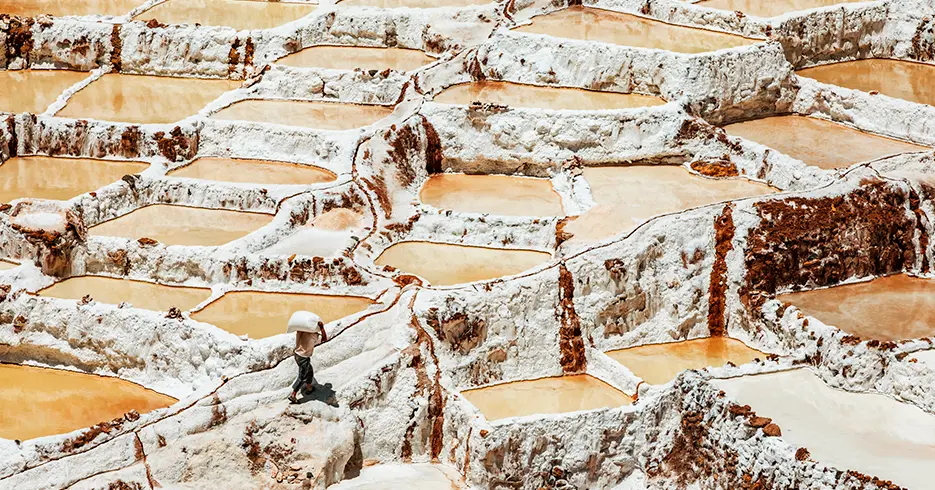 5 Ciudades de Perú que Todo Viajero debe Conocer 4 salineras de maras en cusco, diferentes piscinas llenas de sal y un hombre de la comunidad cargando la sal