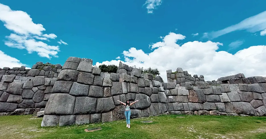 Turista en el centro arqueológico de Sacsayhuaman, con un cielo celeste y la vista de las grandes piedras de la fortaleza inca