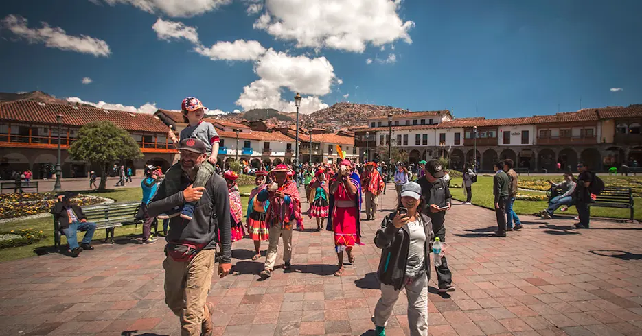 Turistas caminando por la plaza de armas de cusco y personas locales vestidas con trajes típicos, haciendo como un teatro