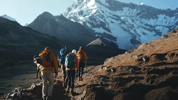 Turistas caminando hacia un nevado, con sus bastones y mochilas por un camino empedrado y vistas de paisajes con nieve