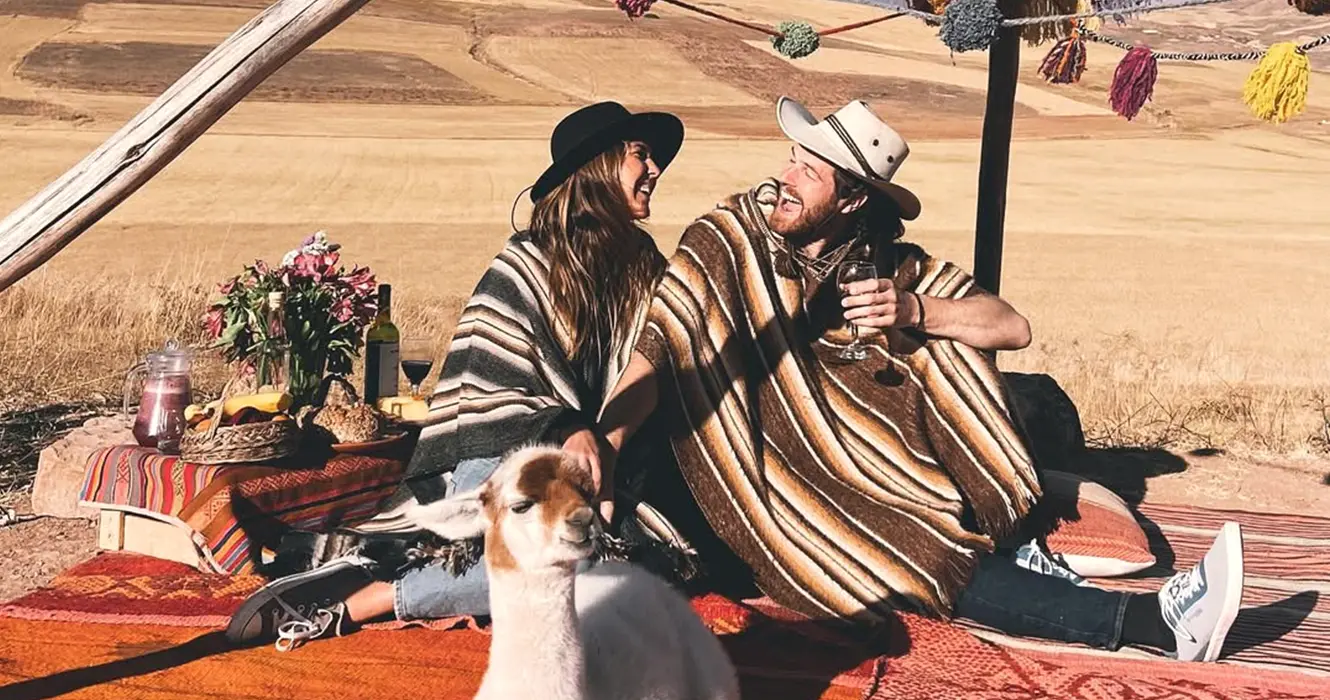Turistas en un pícnic con una llama, tomando vino y con vistas del valle sagrado de los incas en cusco