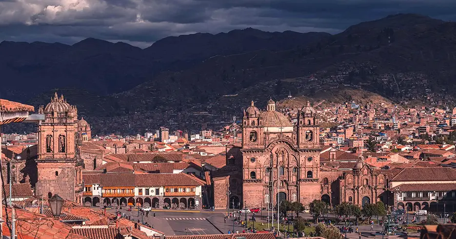 Plaza de armas de cusco, de fondo muchas casas y la vista de montañas y de la iglesia de la catedral y la compañía de Jesús